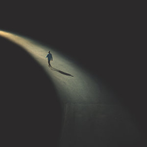 Solitary person walking into the distance along a lit path surrounded by darkness